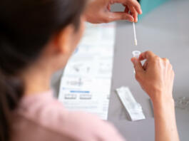 Asian woman using rapid antigen test kit for self test COVID-19 epidemic at home. Adult female place the fabric tip of the swab in the extraction tube and rolling around the tube. COVID-19 pandemic protection concept.