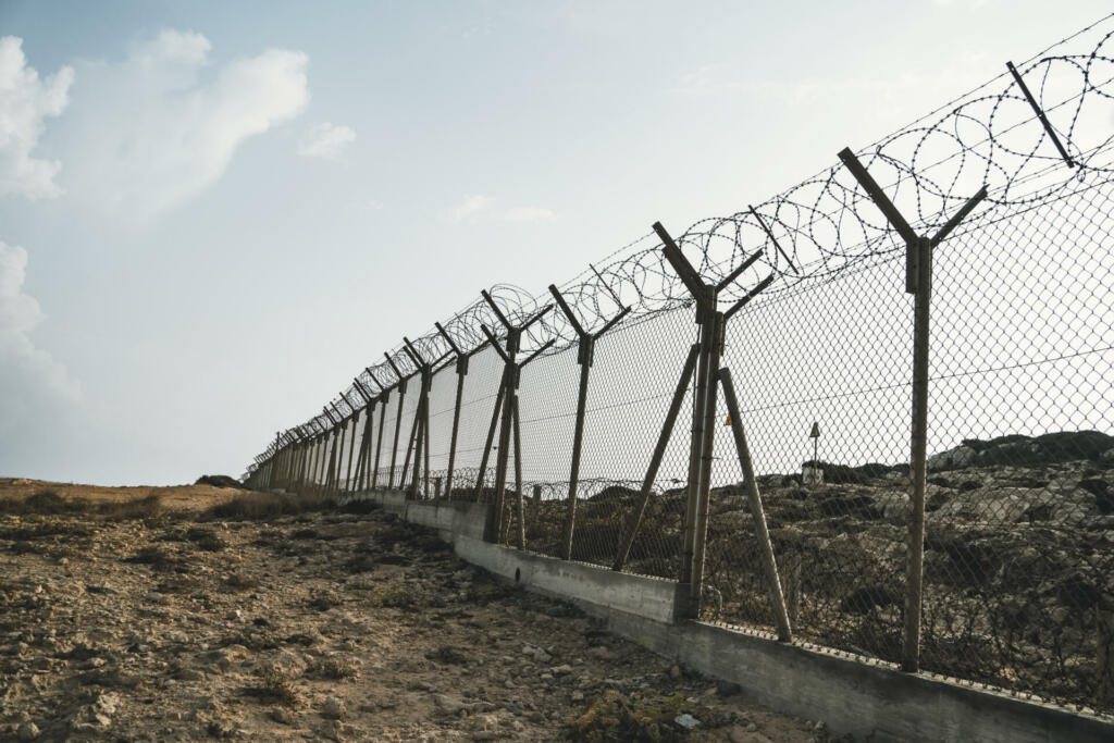barbed wire steel wall against immigations. Wall with barbed wire on the border of 2 countries. Private or closed military zone against the background blue sky.