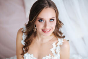 Beautiful bride with long hair in elegant wedding dress and diadem smiling in room in the wedding morning