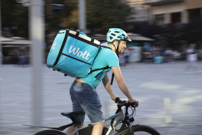 Belgrade, Serbia - June 5, 2021: Wolt delivery food service courier riding a bike on city street on a sunny day