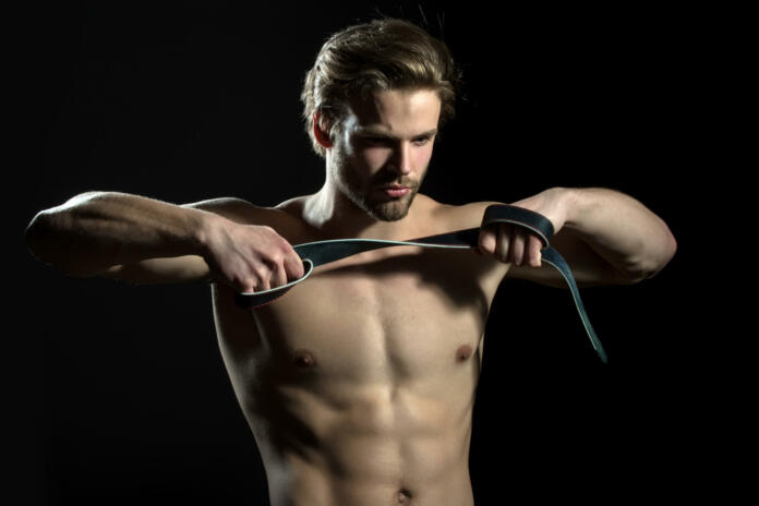 Belt in hands of naked man. The guy does exercises for hands with leather belt. Sexy model for men's accessories. Concentration and meditation in the gym