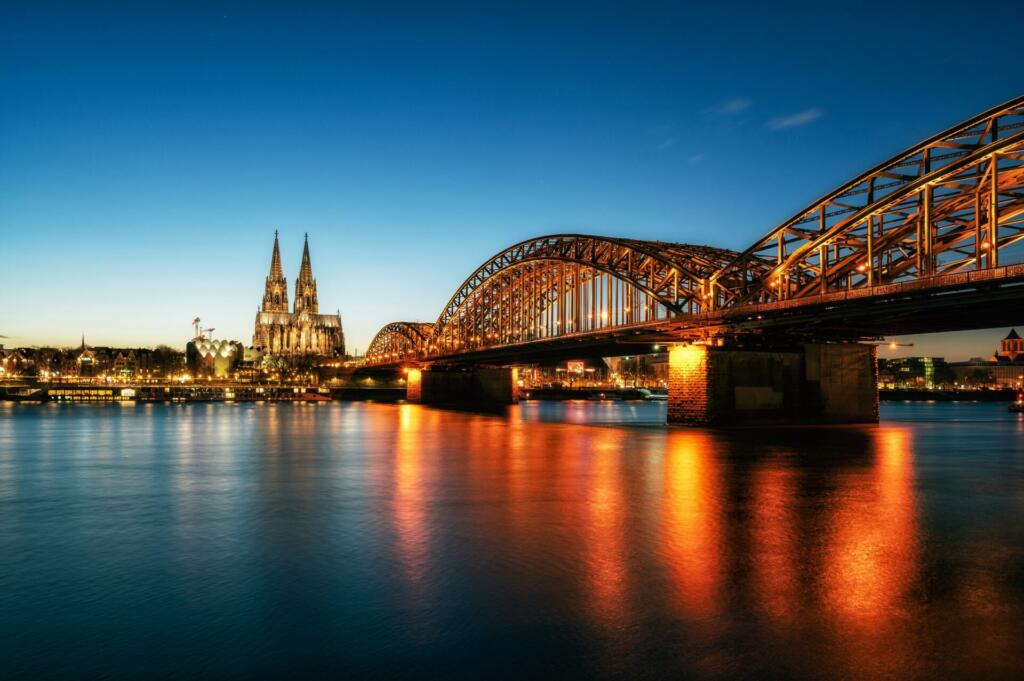 Široka reka, čez katero vodi osvetljen most, v ozadju je katedrala