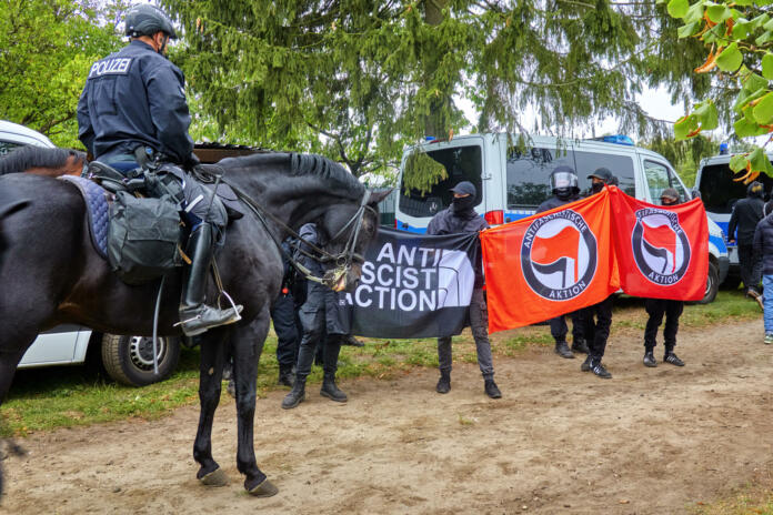 Celle, Germany, September 26, 2020: Policeman on a black horse stands in front of demonstrators carrying banners of Antifa