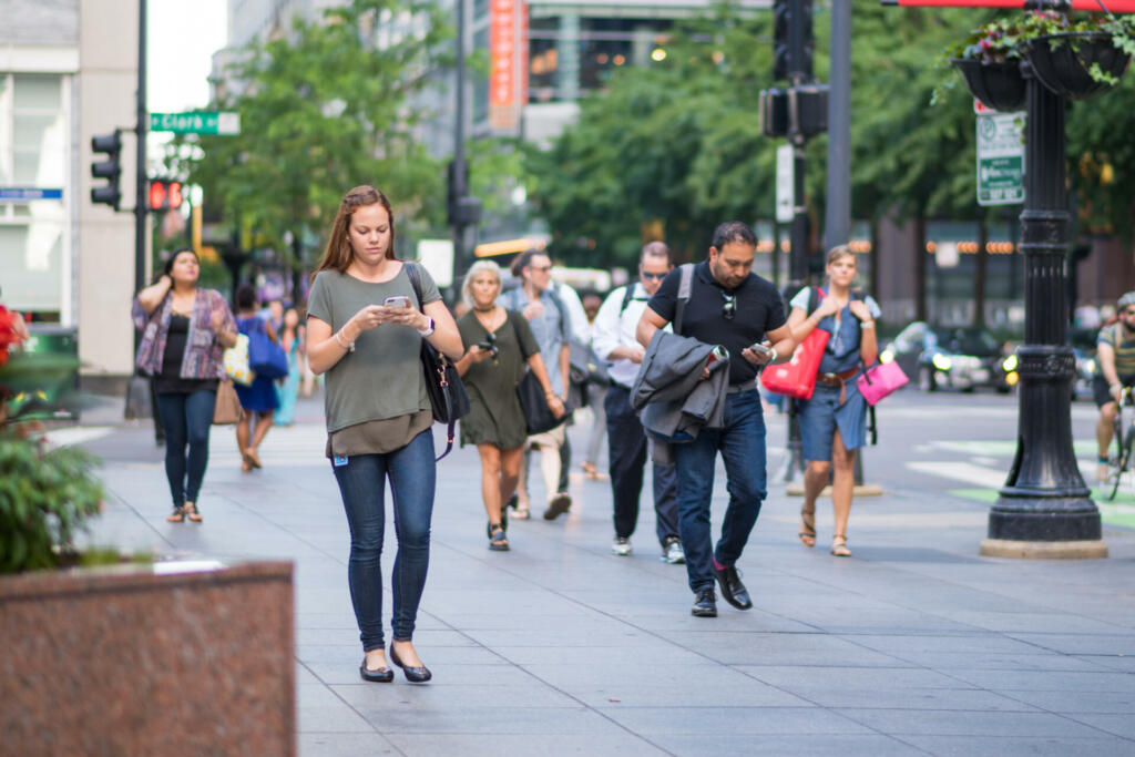 Chicago, IL, June 15, 2017: Young woman checks her phone while walking, downtown Chicago. Cell phones are ubiquitous in the city, and many people text and check social media while walking or commuting