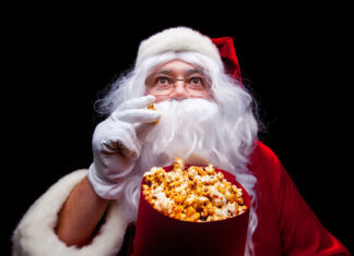 Najboljši božični filmi vseh časov Christmas. Photo of Santa Claus gloved hand With a red bucket with popcorn, on a black background.