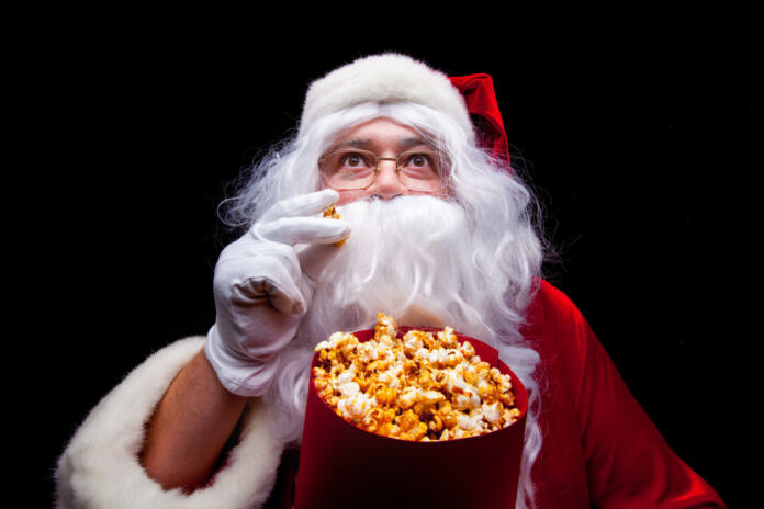 Christmas. Photo of Santa Claus gloved hand With a red bucket with popcorn, on a black background.
