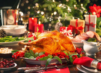 Tradicionalne božične jedi pri nas in po svetu Christmas turkey dinner. Baked turkey garnished with red berries and sage leaves in front of Christmas tree and burning candles