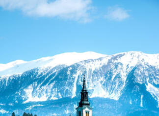 Otoček sredi (rdečega) jezera Clear and blue lake Bled with a church on an islet. Snow-capped mountains in the background