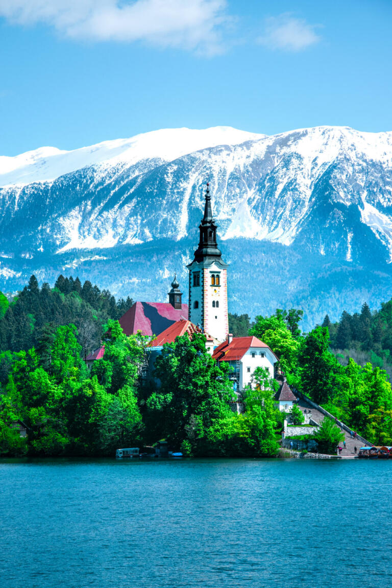 Clear and blue lake Bled with a church on an islet. Snow-capped mountains in the background