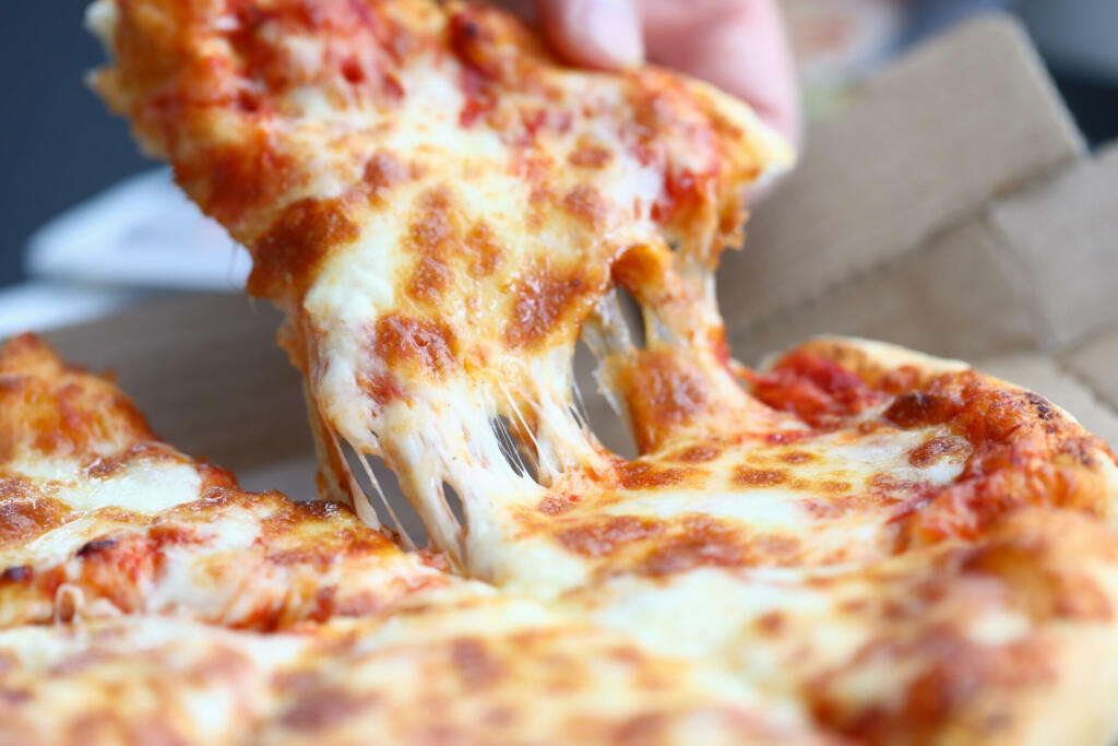 Close-up of person hand taking piece of pizza. Worker having lunch. Cheese pizza with sausage slices. Delicious food and home or office delivery concept