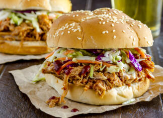 Topli sendviči malo drugače: 10 idej Close up of pulled pork barbeque sandwich with coleslaw sitting on wooden table with glass of beer