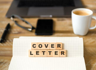 Kako napisati dobro motivacijsko pismo? Closeup on notebook over wood table background, focus on wooden blocks with letters making COVER LETTER words. Business concept image. Laptop, glasses, pen and mobile phone in a defocused background.