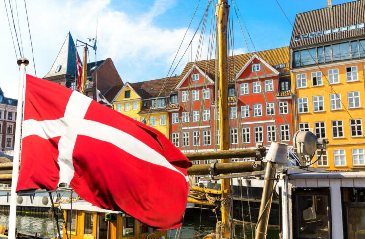 Copenhagen iconic view. Famous old Nyhavn port in the center of Copenhagen, Denmark during summer sunny day with Denmark flag on the foreground