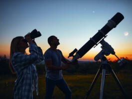 Couple stargazing together with a astronomical telescope.