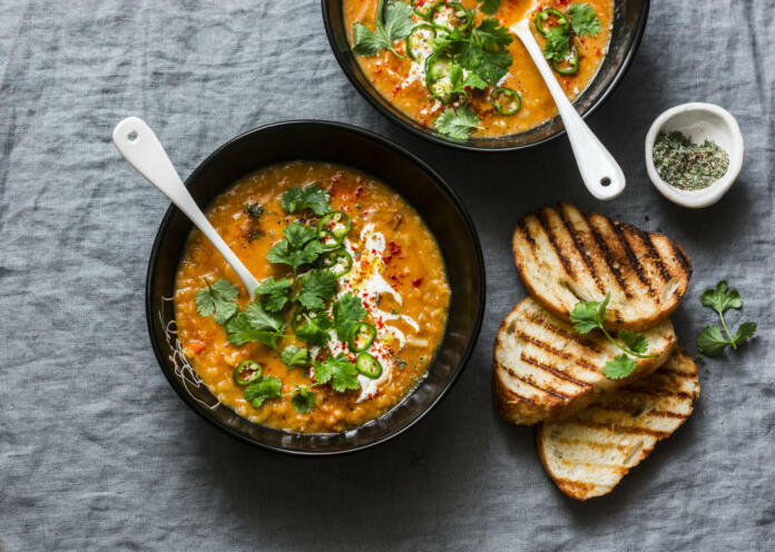 Curried red lentil tomato and coconut soup - delicious vegetarian food on grey background, top view. Flat lay served healthy lunch