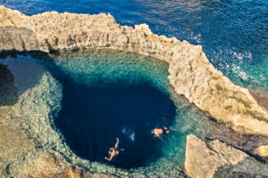 Deep blue hole at the world famous Azure Window in Gozo island - Mediterranean nature wonder in the beautiful Malta - Unrecognizable scuba divers swimming to adventure water cave