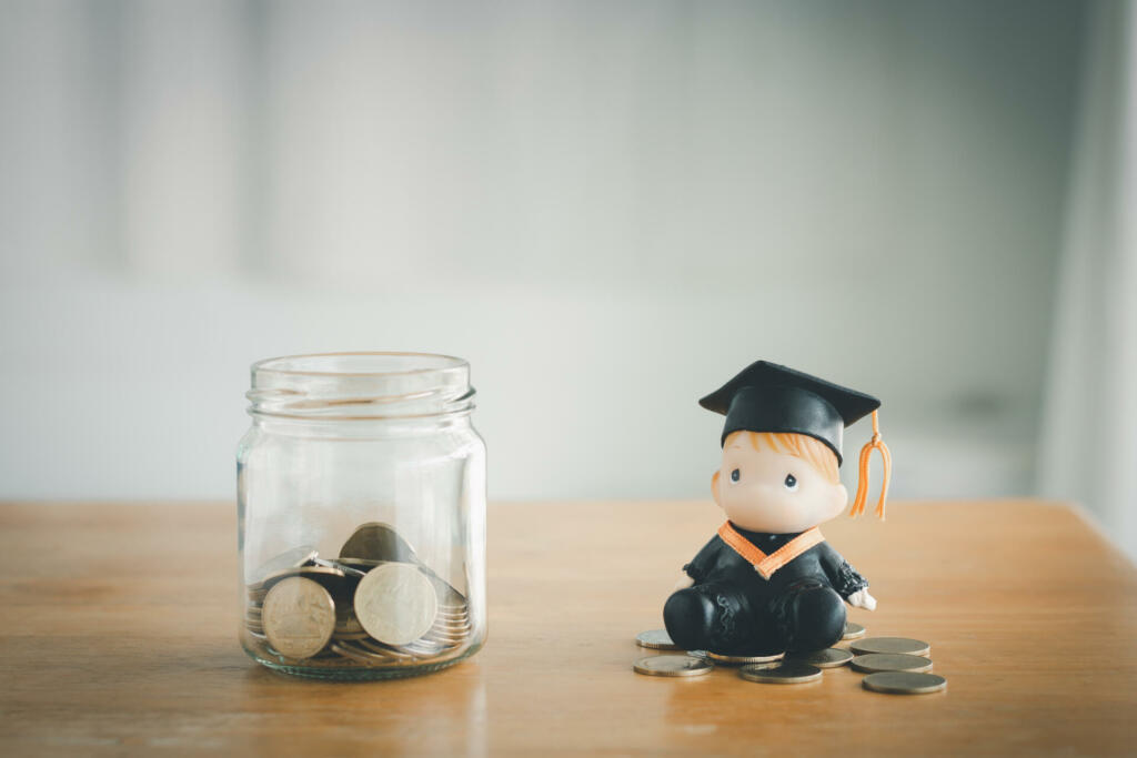 Education savings concept. Coins in a glass jar for education money savings with a graduate doll. Personal financial planning for the future.
