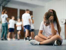 Elementary student sitting away from her classmates and teacher and feeling sad during physical education class.
