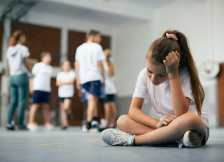 Nenapisane ovire in šola, ki jih lahko preseže Elementary student sitting away from her classmates and teacher and feeling sad during physical education class.