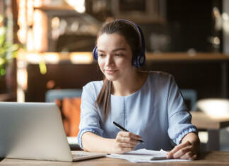 Pouk na daljavo ostaja tudi v novem šolskem letu Focused woman wearing headphones using laptop in cafe, writing notes, attractive female student learning language, watching online webinar, listening audio course, e-learning education concept