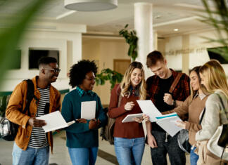 Študentje vsaj deloma na fakultete, študij izključno na daljavo le v izrednih primerih Happy female student showing test results to her friends while standing in a lobby.