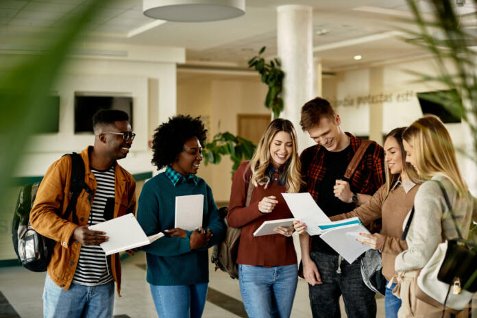 Happy female student showing test results to her friends while standing in a lobby.