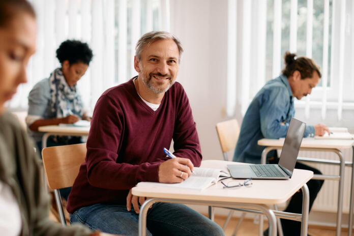 Happy mature man attending a lecture and writing notes while looking at camera.