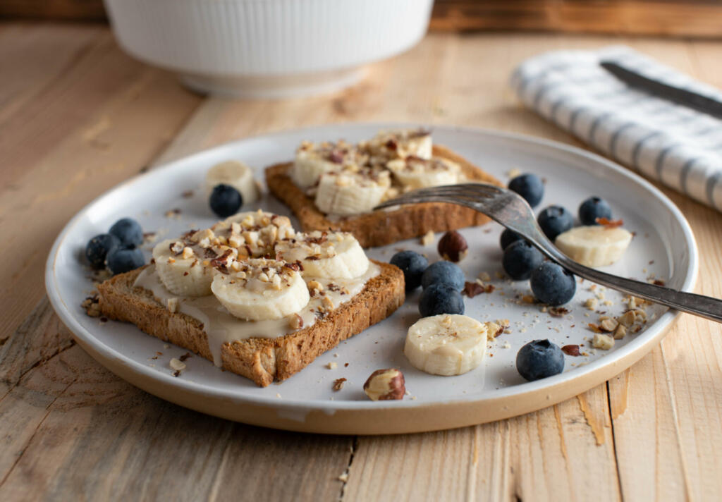 Healthy and clean eating breakfast plate  for power and energy with whole grain toast topped with almond butter, bananas and hazelnuts. Served with fresh blueberries isolated on wooden table. Ready to eat
