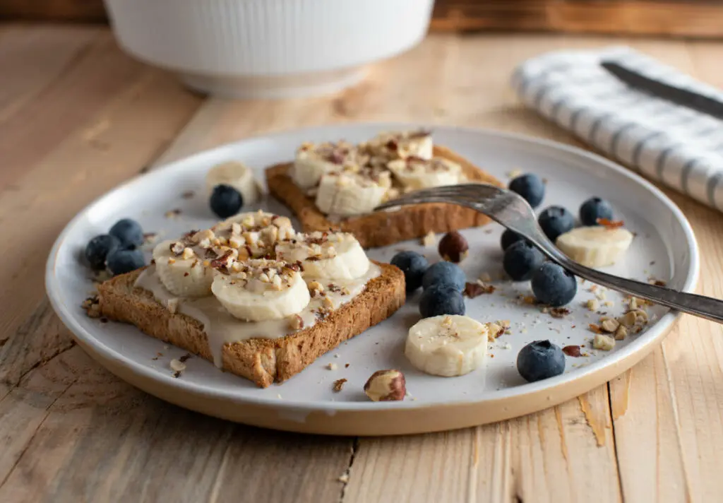 Healthy and clean eating breakfast plate for power and energy with whole grain toast topped with almond butter, bananas and hazelnuts. Served with fresh blueberries isolated on wooden table. Ready to eat