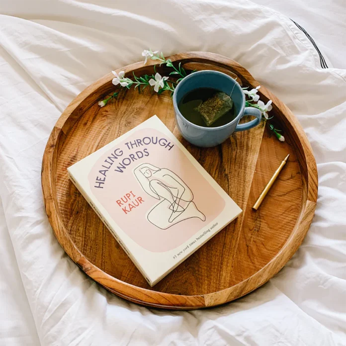Knjiga Healing through words na lesenem pladnju s čajem, na postelji
