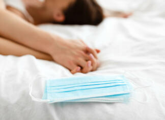 Najboljši seks položaji za čas v karanteni Love And Dating During Covid-19 Pandemic. Protective Face Masks Lying Near Passionate Couple Holding Hands Having Sex In Bed Indoors. Conceptual Shot. Selective Focus, Shallow Depth