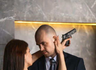 Najbolj seksi filmi vseh časov Man and woman with weapons. Elegant guy in a suit hugs beautiful girl in a black dress holding a gun