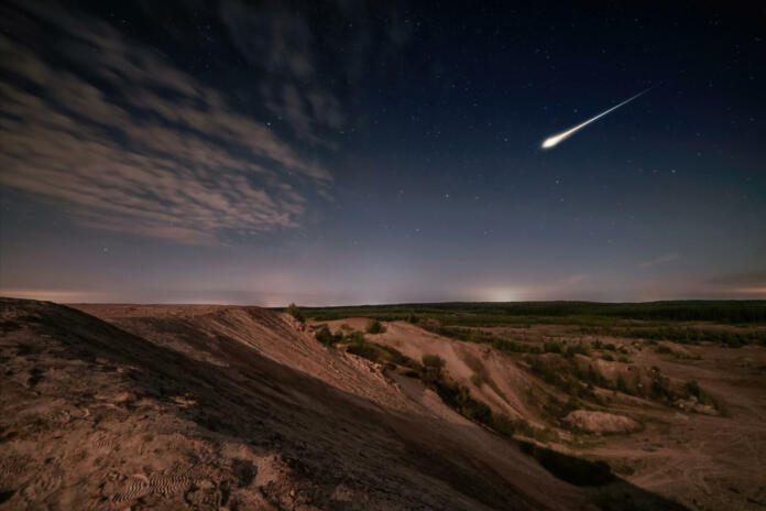 Meteor over sand hills and forest in moon light and starry sky. Long exposure night scene