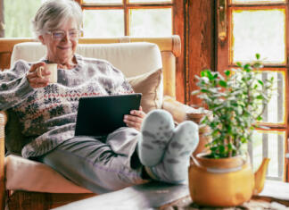 Digitalni bon 22: Znani so izvajalci izobraževanj za starejše od 55 let Old senior woman sitting at home on armchair using digital tablet wearing a warm sweater and eyeglasses. Comfortable living room, wooden rustic windows