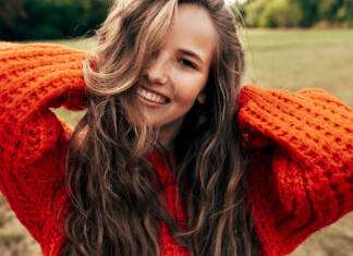 Top 3 domače maske za lase Outdoor portrait of a smiling young woman wearing a knitted orange sweater posing on nature background. The beautiful female has a joyful expression, resting in the park.
