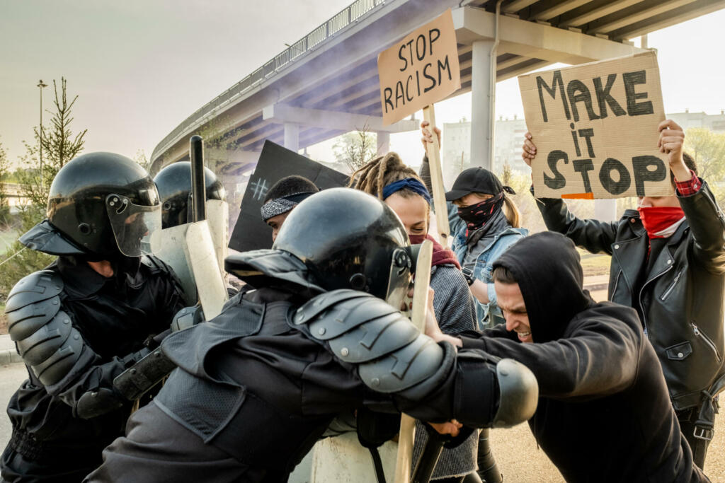 Riot police in helmets pushing protestors with shields while fighting against them at rally