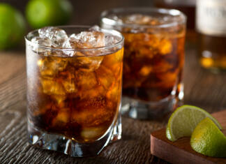 5 preprostih pivskih iger Rum and cola Cuba libre with lime and ice on a wooden bar top.