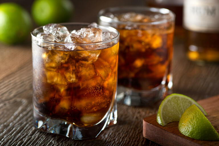 Rum and cola Cuba libre with lime and ice on a wooden bar top.