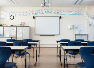 »Študenti želimo nazaj na fakultete« School desk and chairs in empty modern classroom. Empty class room with white board and projector in elementary school. Primary classroom with smartboard and alphabet on wall.