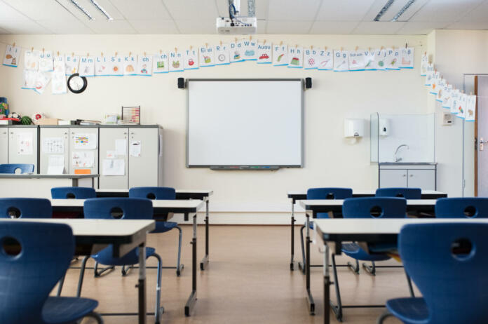 School desk and chairs in empty modern classroom. Empty class room with white board and projector in elementary school. Primary classroom with smartboard and alphabet on wall.