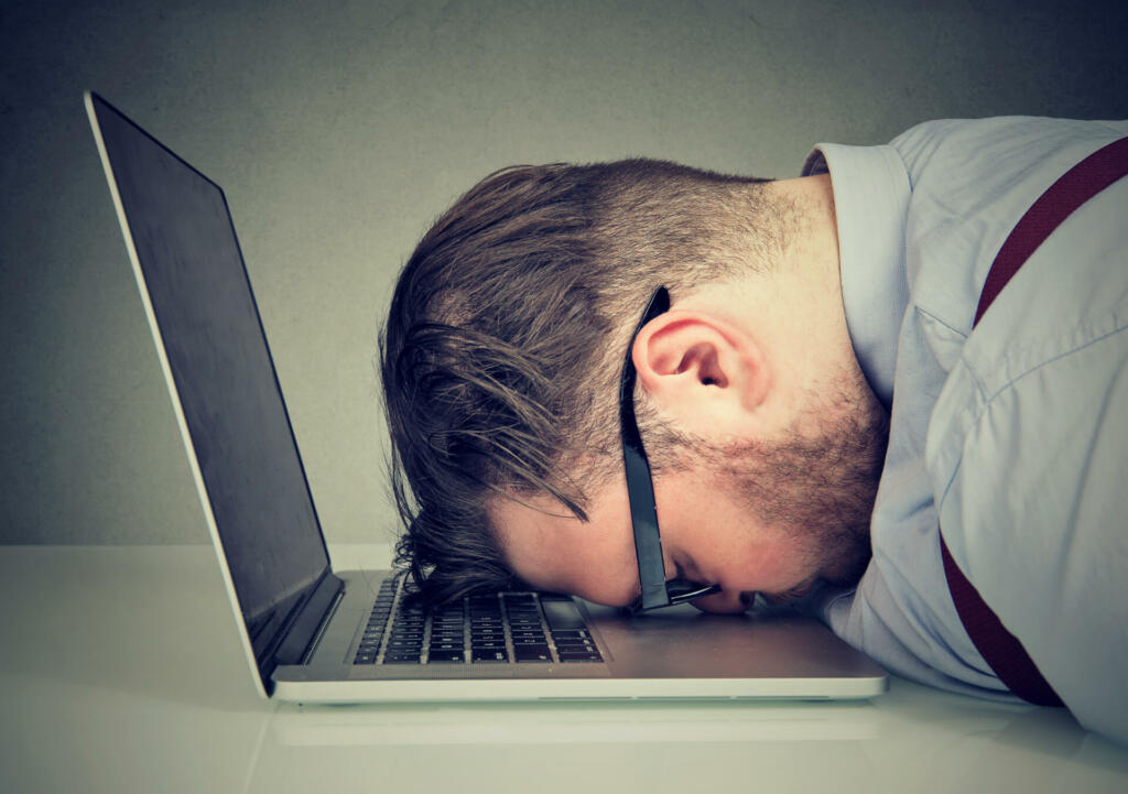 Side view of chubby man looking broken while lying on top of laptop.