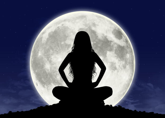 silhouette of a young beautiful woman with long hair in meditation posture with the full moon on the background, some graphics are provided by Nasa
