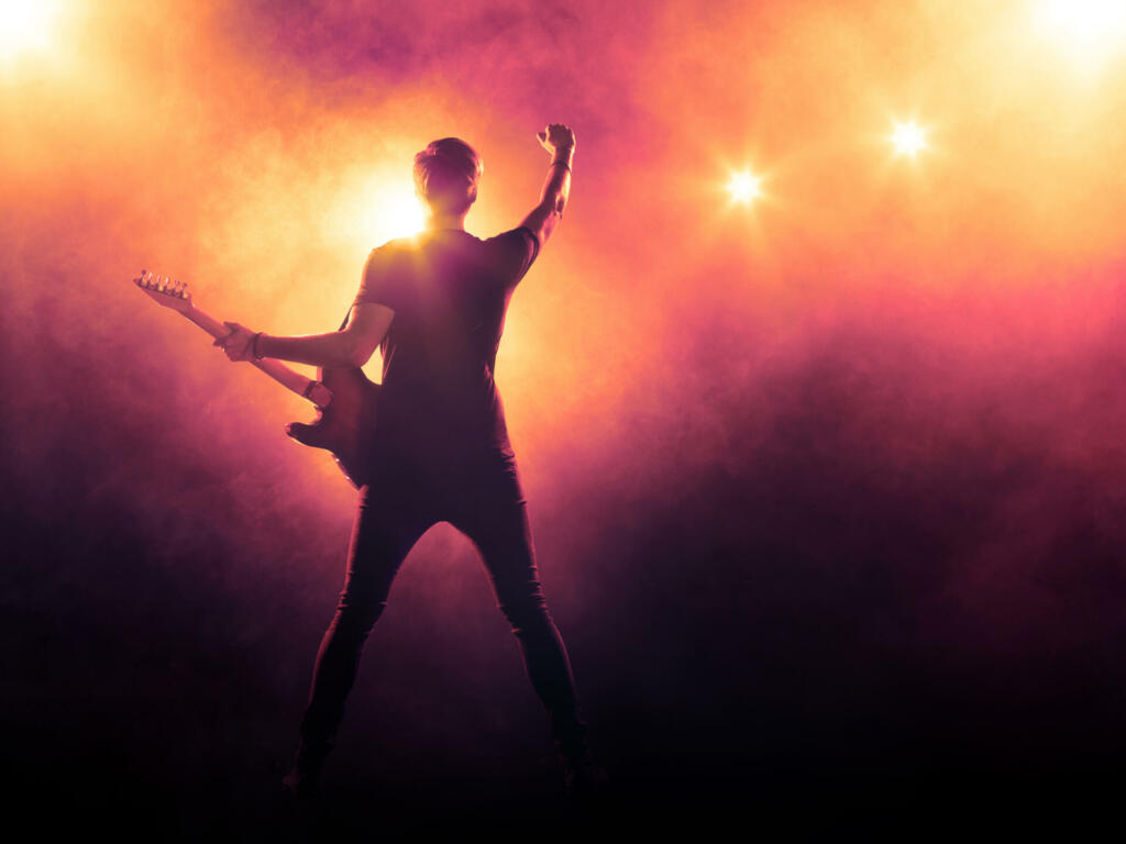 Silhouette of guitar player on stage on orange background with smoke and spotlights