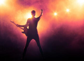 Zgodovina Rock’n’rolla Silhouette of guitar player on stage on orange background with smoke and spotlights