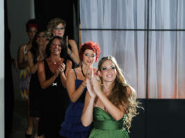 Six models parade down the runway, clapping, after a great fashion show.