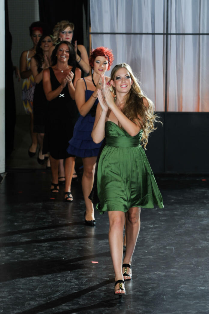 Six models parade down the runway, clapping, after a great fashion show.