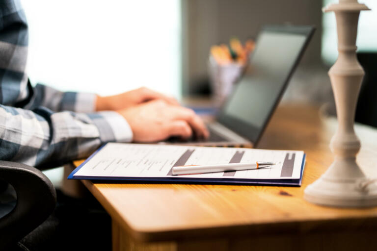 Survey form, customer satisfaction feedback poll, resume for job application or for college. Man writing with laptop.  Home or car insurance contract. Paper sheet and pen on desk.