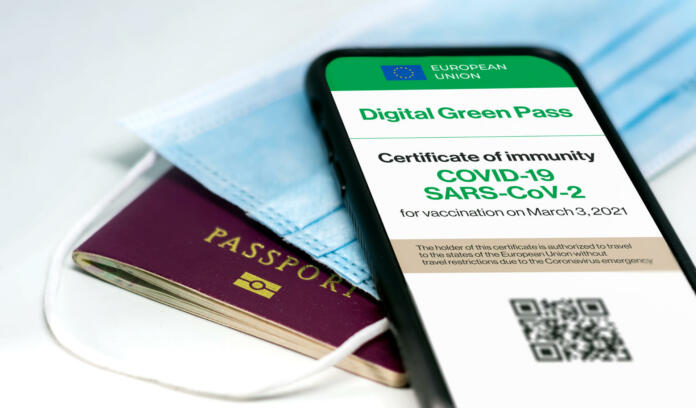 The digital green pass of the european union with the QR code on the screen of a mobile phone over a surgical mask and a passport. Immunity from Covid-19. Travel without restrictions.