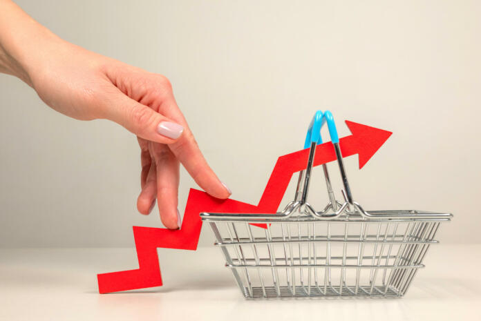 The fingers of a woman's hand step up the arrow of a chart lying on a shopping basket. Crisis and rising commodity prices concept