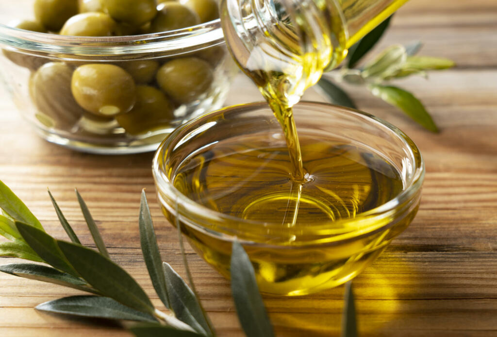 The moment olive oil is poured into a glass bowl set against a wooden background